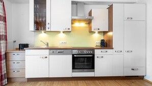 Una cocina compacta con muebles blancos, horno integrado, cafetera y tostadora.