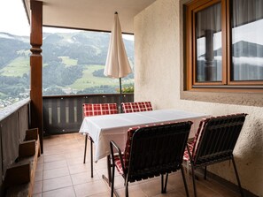 A balcony with a table and chairs, a view of the countryside, and a window with curtains. - Appartements Sonnberg - Top 5 (Bad Hofgastein)
