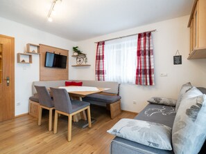 A compact living space with a sofa, a dining table, and chairs. A television is mounted on the wall, and there are shelves with decorative items. - Appartements Sonnberg - Top 5 (Bad Hofgastein)