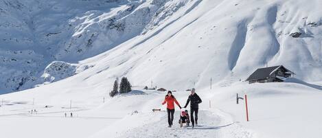 Un sentier de montagne enneigé, avec un chalet en bois et un télésiège en arrière-plan.