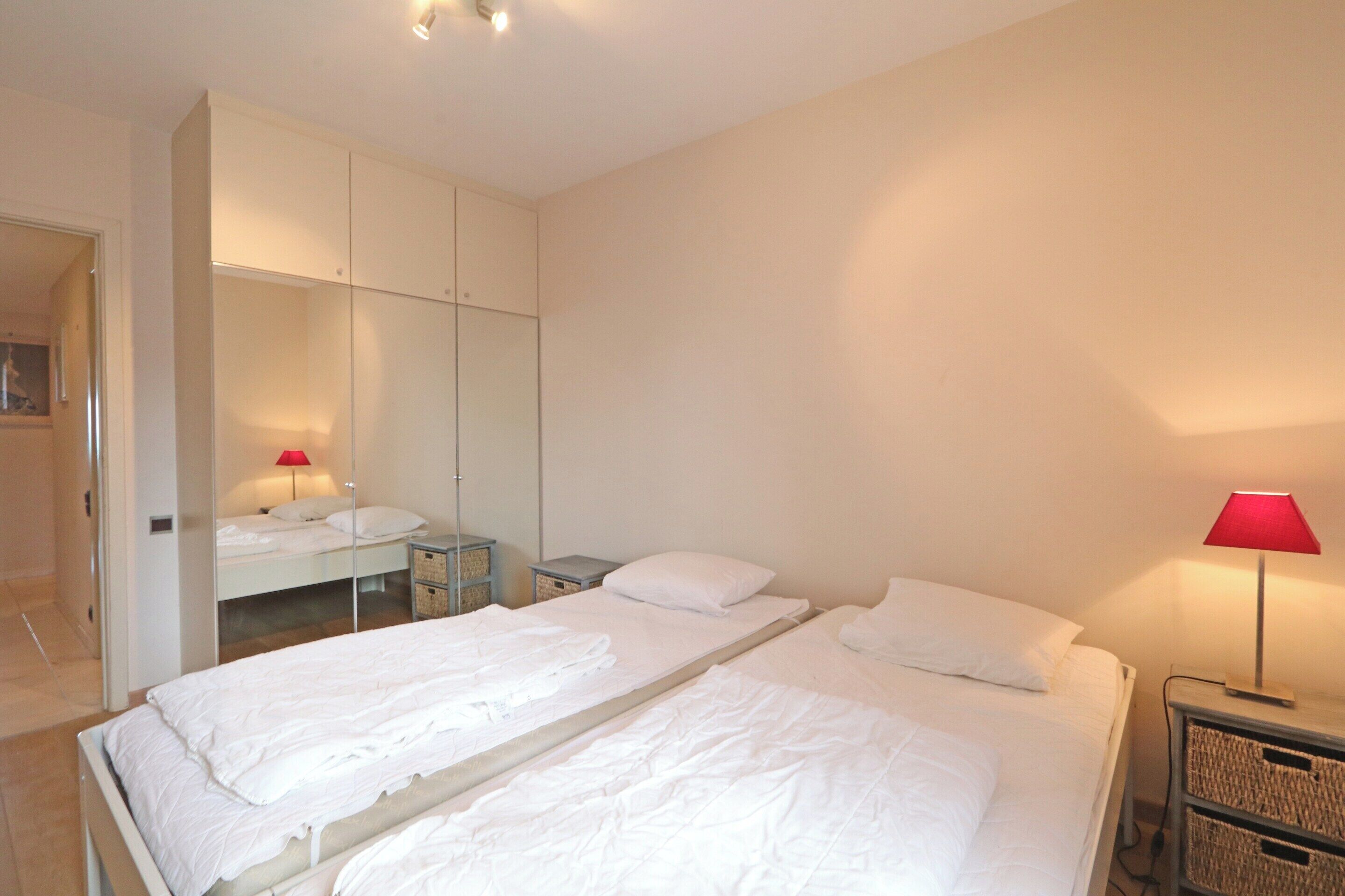 Een hotelkamer met twee bedden, een kledingkast, een nachtkastje en een lamp.