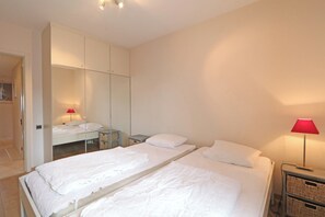A hotel room with two beds, a wardrobe, a bedside table, and a lamp. - Sea View Apartment in the Heart of Zoute (Knokke-Heist)