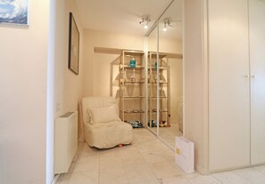 A room with a white chair, a glass cabinet with shelves, and a white door. - Sea View Apartment in the Heart of Zoute (Knokke-Heist)