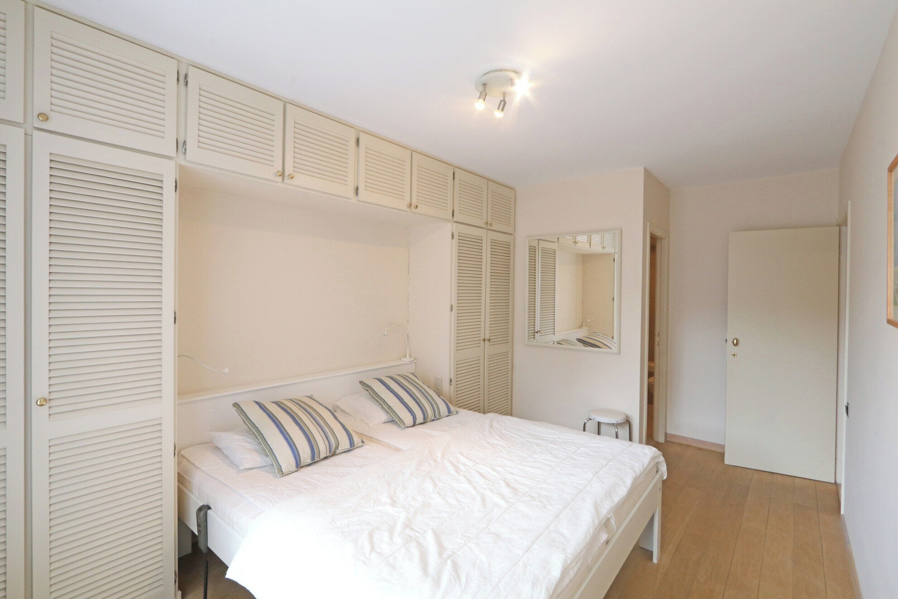 Un dormitorio con cama, mesitas de noche, un espejo y un armario con puertas batientes.