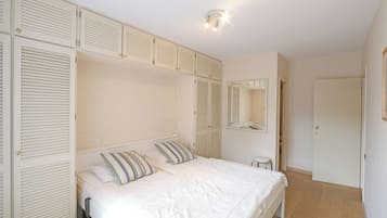Un dormitorio con cama, mesitas de noche, un espejo y un armario con puertas batientes.