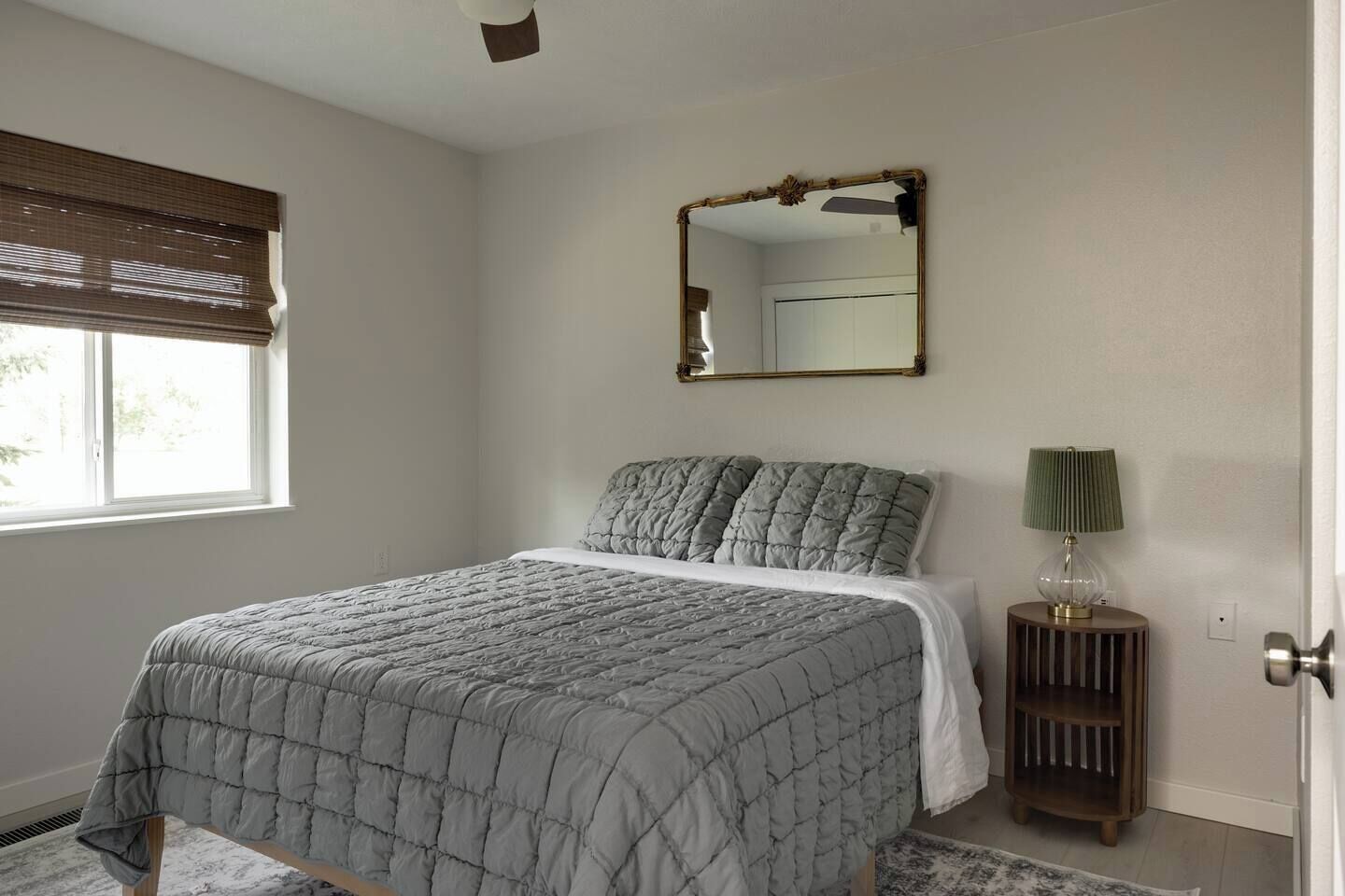 A bedroom with a bed, a bedside lamp, a mirror, and a window with blinds.