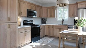 Une cuisine moderne avec des meubles en bois, des appareils électroménagers en acier inoxydable, un coin repas avec une table et des chaises, et un luminaire suspendu.