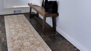 Un couloir avec une porte blanche, un banc agrémenté de coussins et un tapis à motifs.
