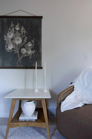 Una habitación con una mesa blanca, una jarrón blanco y un libro titulado 'HOME THERAPY' sobre una estantería de madera.