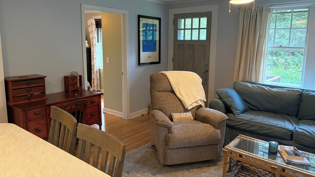 A living room with a wooden desk, a cushioned armchair, a sofa, and a glass coffee table.