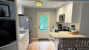 A modern kitchen with white cabinetry, a built-in microwave, a refrigerator, and a wooden dining table with chairs.
