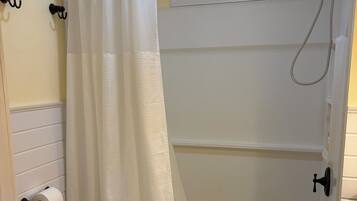 A bathroom with a toilet, a shower with a glass door, a towel rack, and a window above the shower.