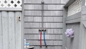 A small, enclosed outdoor area with a stone wall, a wooden fence, and a metal hose attached to the wall.