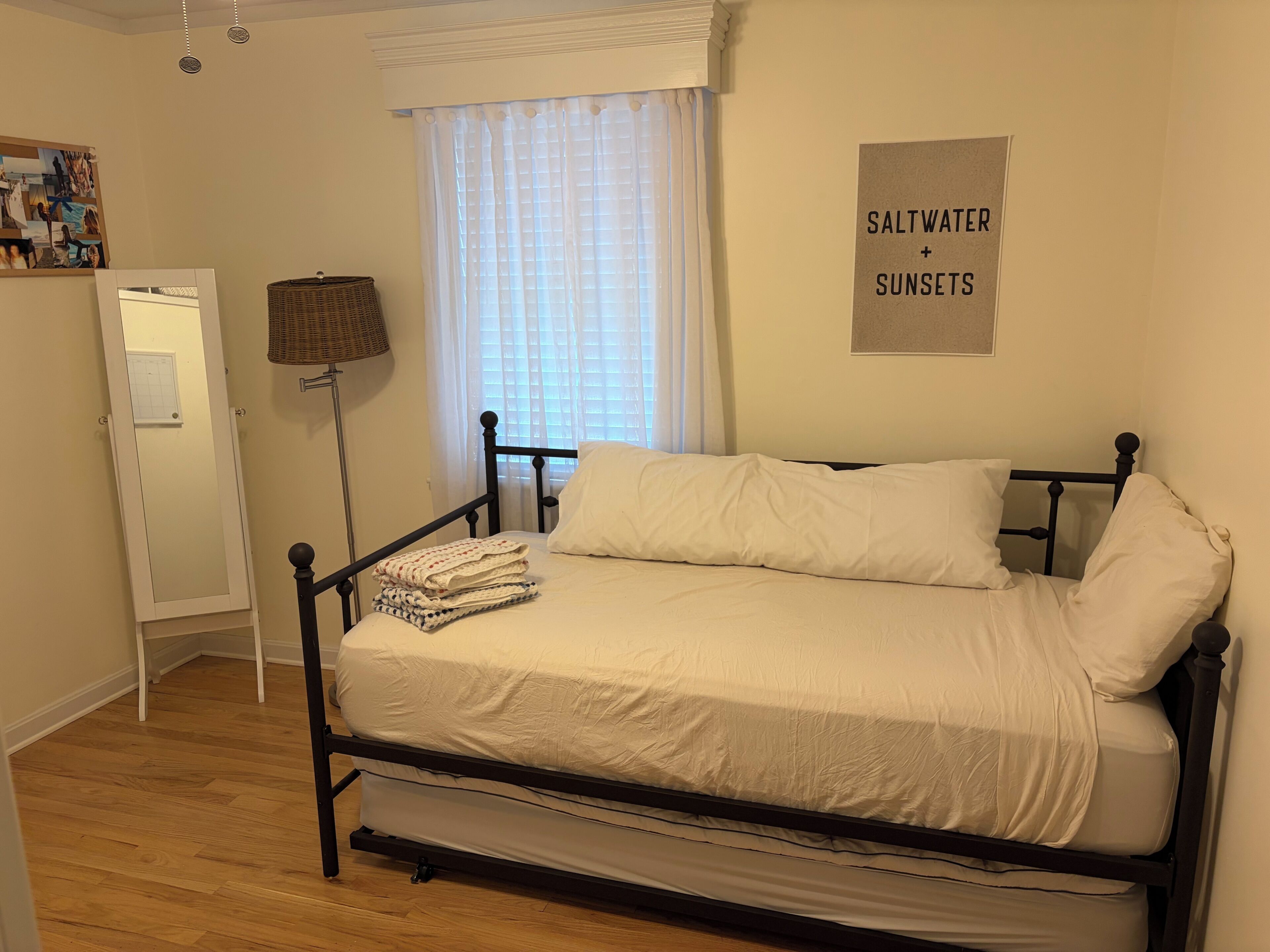 A bedroom with a bed, a window with curtains, a wall-mounted sign, and a floor lamp.