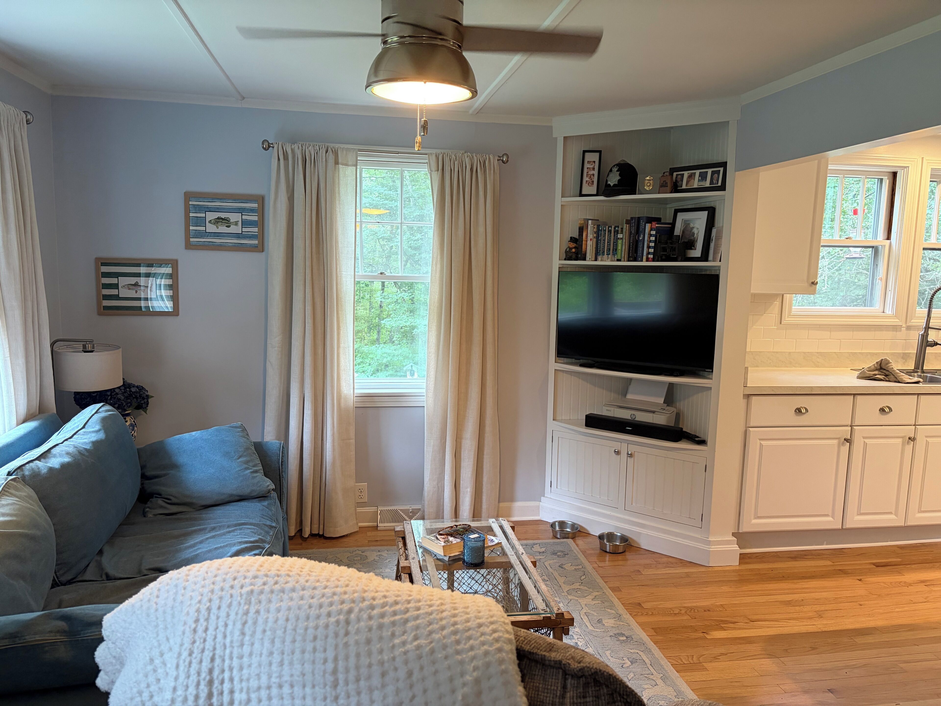 A living room with a sofa, a television, and a kitchen area with cabinets and a window.