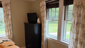 A bedroom with a bed, a dresser, a television on top of the dresser, and a window with curtains.