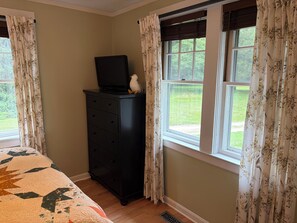 A bedroom with a bed, a dresser, a television on top of the dresser, and a window with curtains.