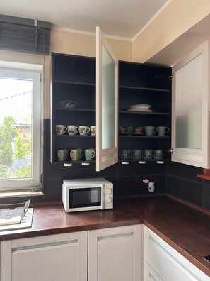 A kitchen with a microwave, open cabinets with dishes, and a window. - A spacious house with a garden by the sea, close to the beach and the pier. (Mosty)