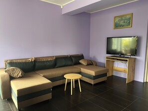 A modern living room with a sectional sofa, a small round table, and a flat-screen TV on a wooden stand. - A spacious house with a garden by the sea, close to the beach and the pier. (Mosty)