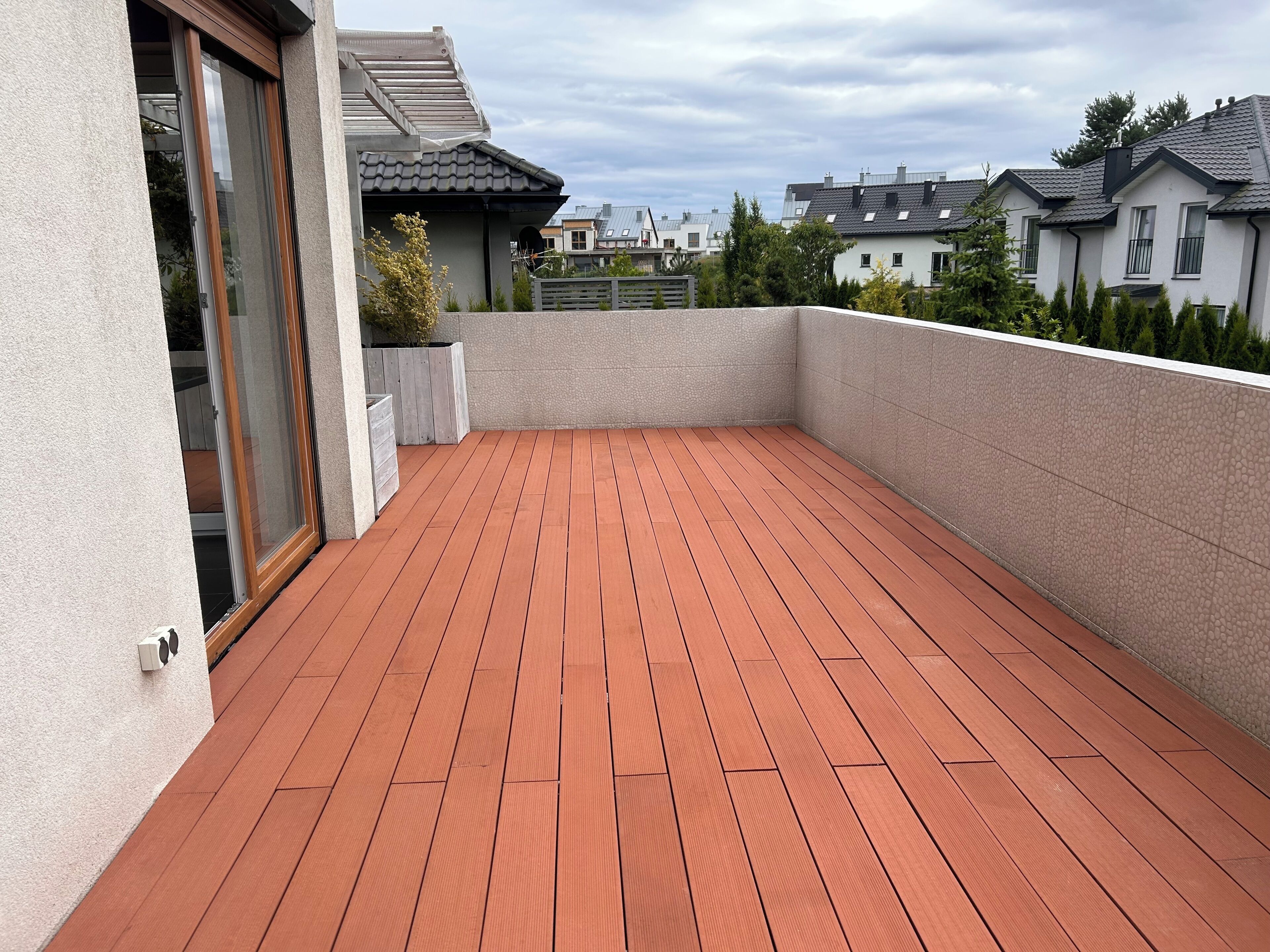 A rooftop deck with a wooden floor, surrounded by walls and a view of neighboring houses.