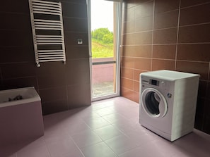A laundry room with a washing machine, a drying rack, and a window with a view of greenery. - A spacious house with a garden by the sea, close to the beach and the pier. (Mosty)
