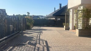 A paved driveway leading to a gated entrance with a metal fence and a building with a tiled roof. - A spacious house with a garden by the sea, close to the beach and the pier. (Mosty)