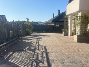 A paved driveway leading to a gated entrance with a metal fence and a building with a tiled roof. - A spacious house with a garden by the sea, close to the beach and the pier. (Mosty)