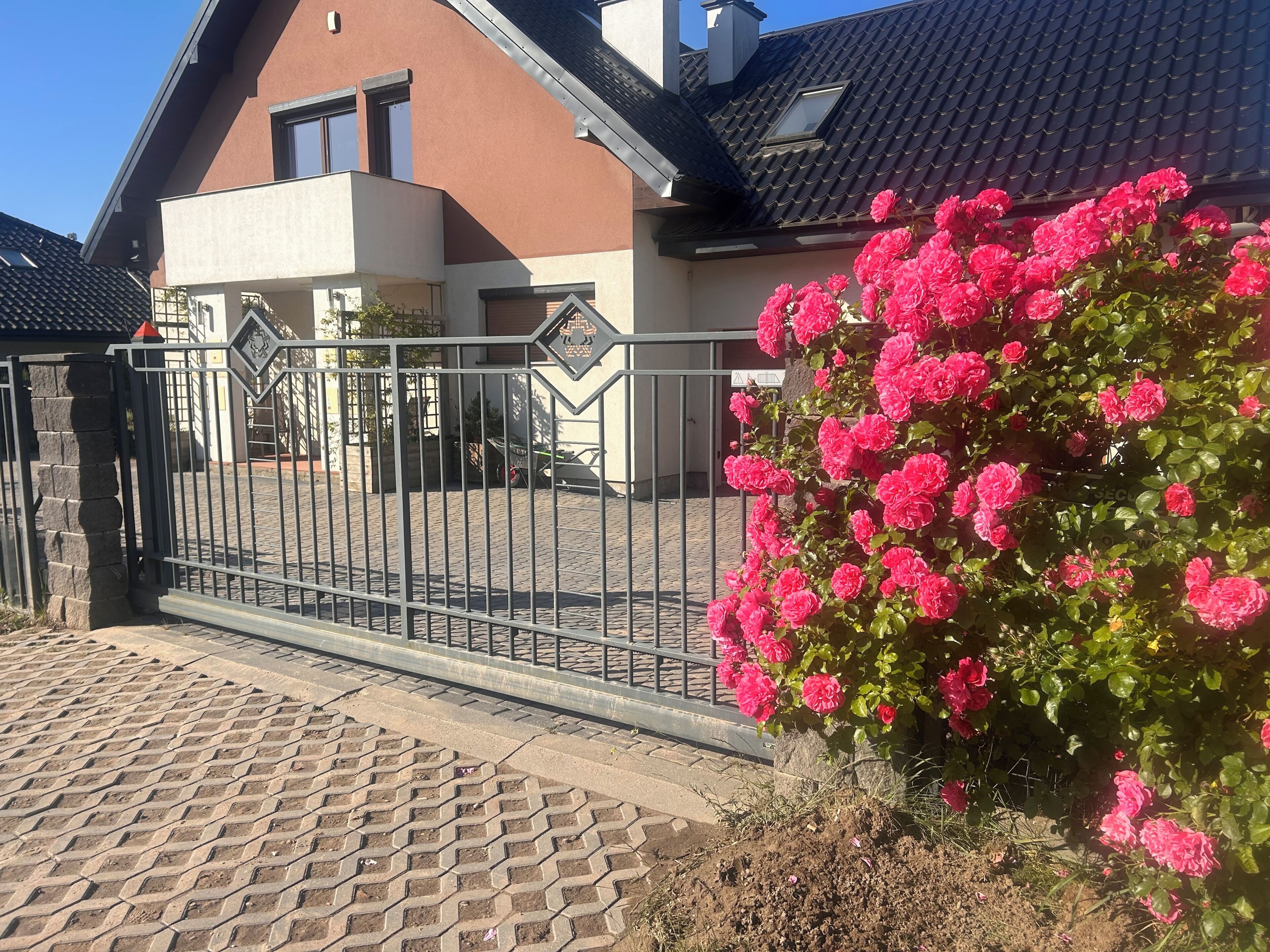 Ein Wohngebäude mit befestigter Auffahrt, einem Metallgitter und einem Busch mit rosafarbenen Blüten.