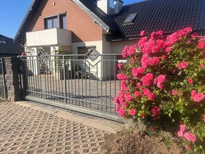 A residential building with a paved driveway, a metal gate, and a bush of pink flowers. - A spacious house with a garden by the sea, close to the beach and the pier. (Mosty)