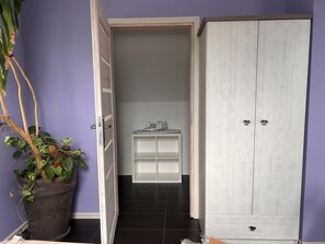 Un couloir avec une plante en pot, une armoire blanche et une petite table avec un fer à repasser.
