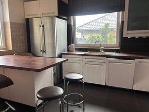 A modern kitchen with a built-in refrigerator, a window with a view of the outside, and a bar area with stools. - A spacious house with a garden by the sea, close to the beach and the pier. (Mosty)