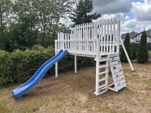 Une aire de jeux avec un toboggan bleu et une structure d’escalade blanche.