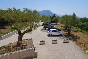A parking area with cars and trees, a clear sky, and a mountain in the background.