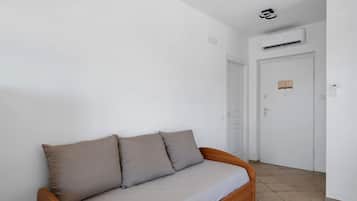 A room with a sofa, a door, and an air conditioning unit.