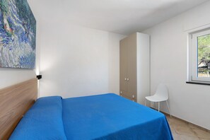 Un dormitorio con cama, armario, silla y ventana.