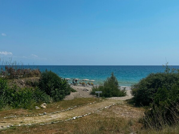 Un camino bordeando la playa, con sombrillas y sillas de descanso.