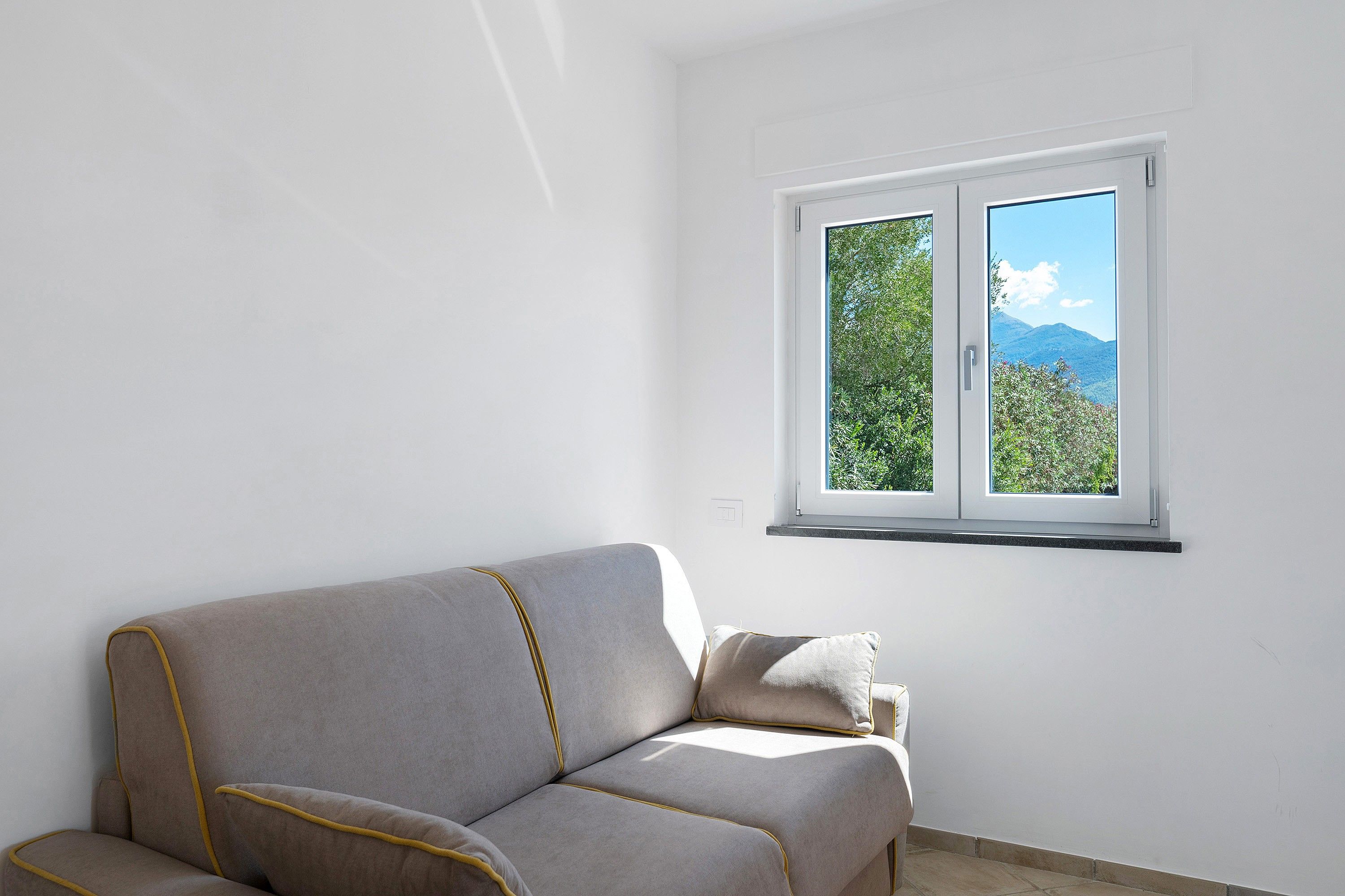 Una stanza con un divano e una finestra vista alberi e montagne.