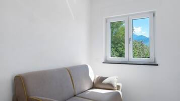 Una stanza con un divano e una finestra vista alberi e montagne.