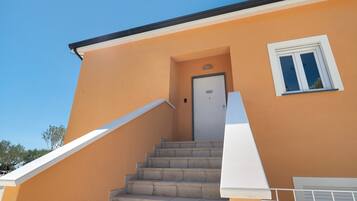 Un escalier menant à une porte surmontée d’une fenêtre, le tout adossé à un immeuble à la façade sobre.