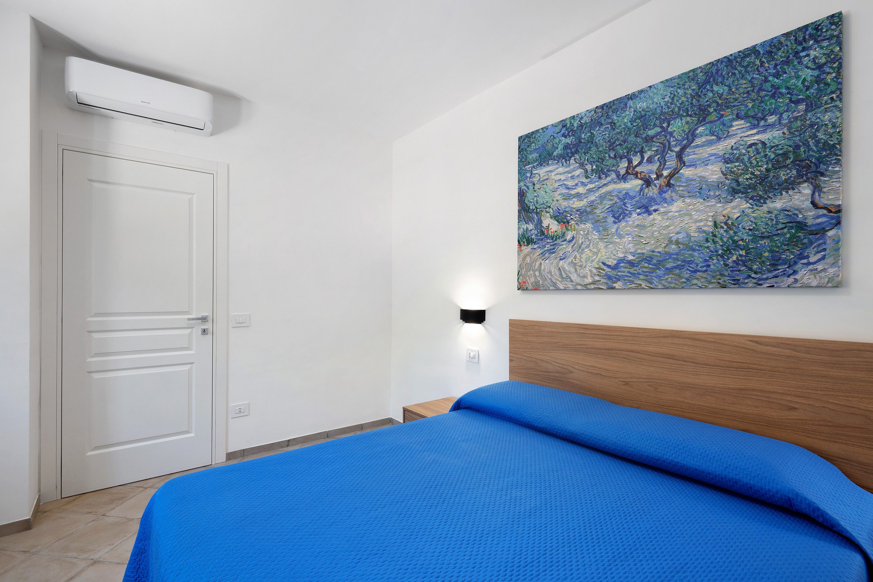 Une chambre d’hôtel avec un lit, un tableau au mur, une porte et un appareil de climatisation.