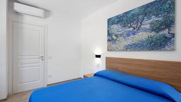 Une chambre d’hôtel avec un lit, un tableau au mur, une porte et un appareil de climatisation.