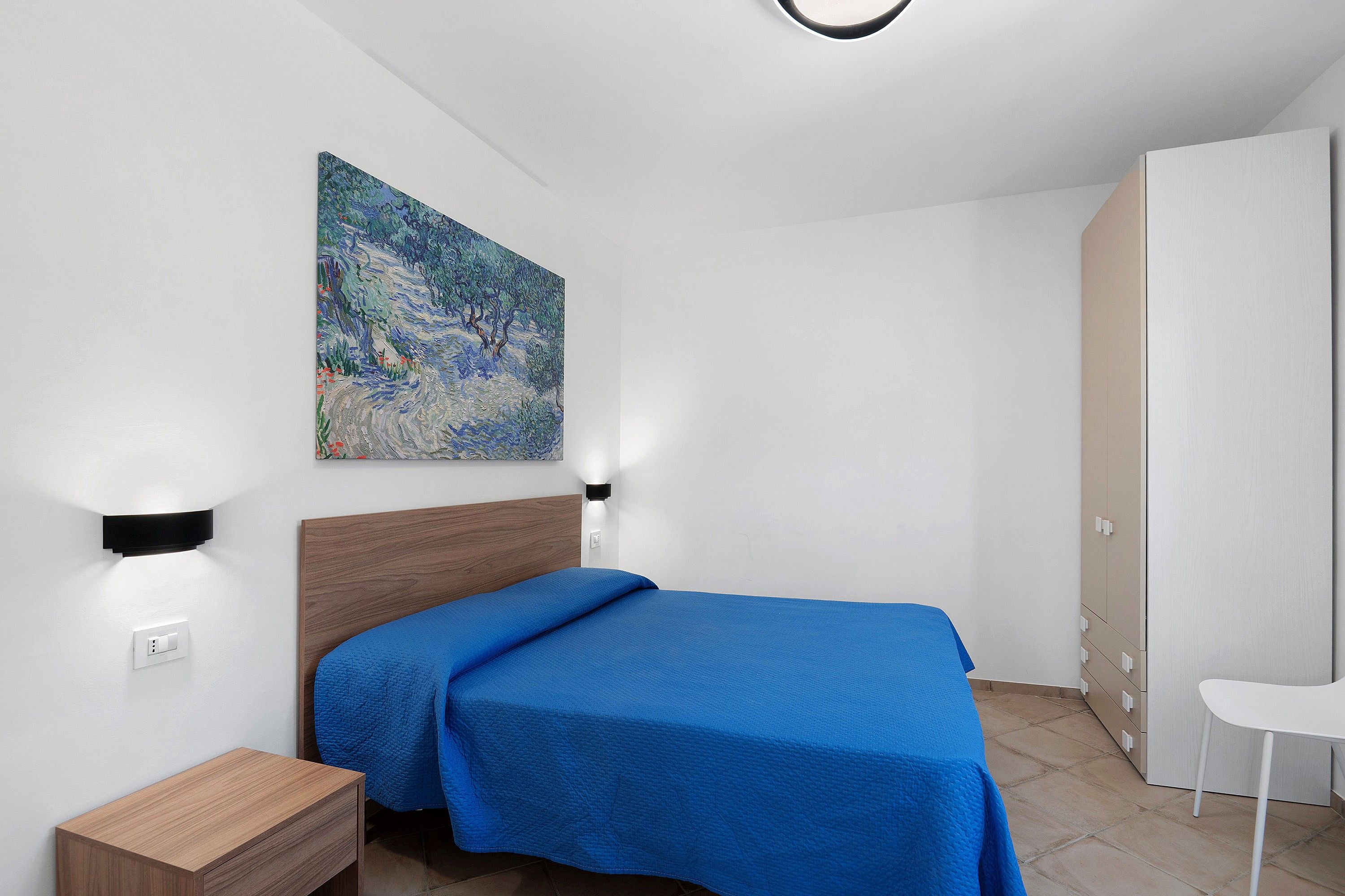 Une chambre à coucher comprenant un lit, une table de chevet, une lampe fixée au mur et un tableau.