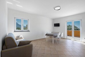 Una sala de estar moderna con un sofá, una mesa de comedor con sillas, un televisor montado en la pared y un balcón con vistas.