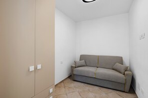Habitació petita amb tons neutres, un sofà, un armari i un interruptor a la paret.