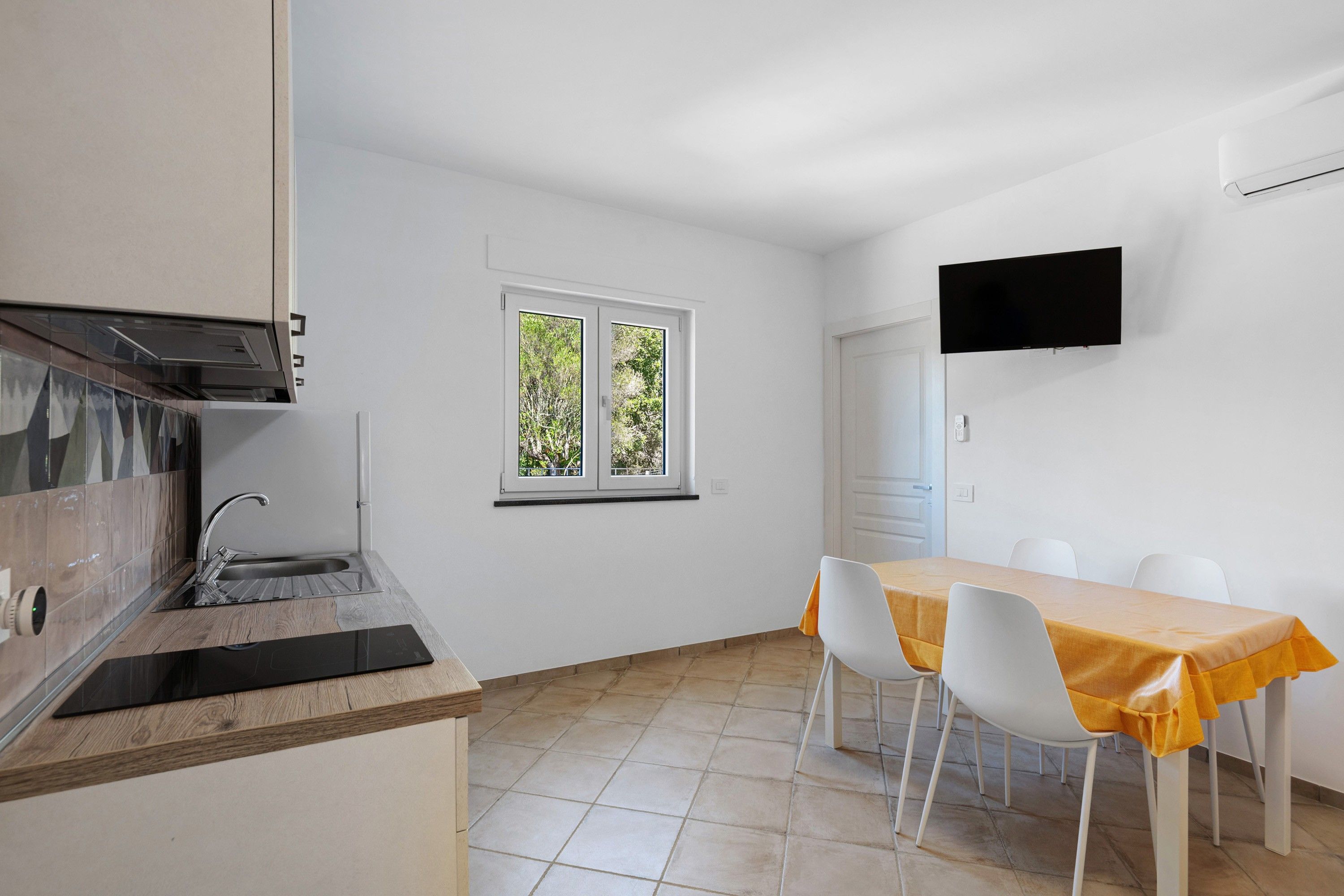 Eine moderne Küche mit eingebautem Ofen und Spüle, ein Essbereich mit Tisch und Stühlen sowie ein an der Wand befestigter Fernseher.