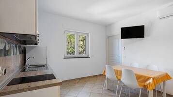 Eine moderne Küche mit eingebautem Ofen und Spüle, ein Essbereich mit Tisch und Stühlen sowie ein an der Wand befestigter Fernseher.