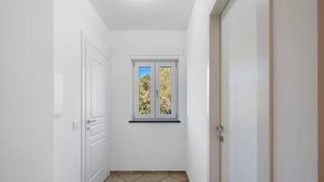 A narrow hallway with white walls, a window with a view of trees, and a door on the right.