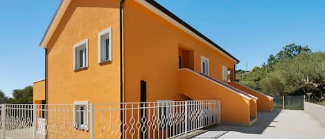 A two-story building with a flat roof, white window frames, and a white metal fence.