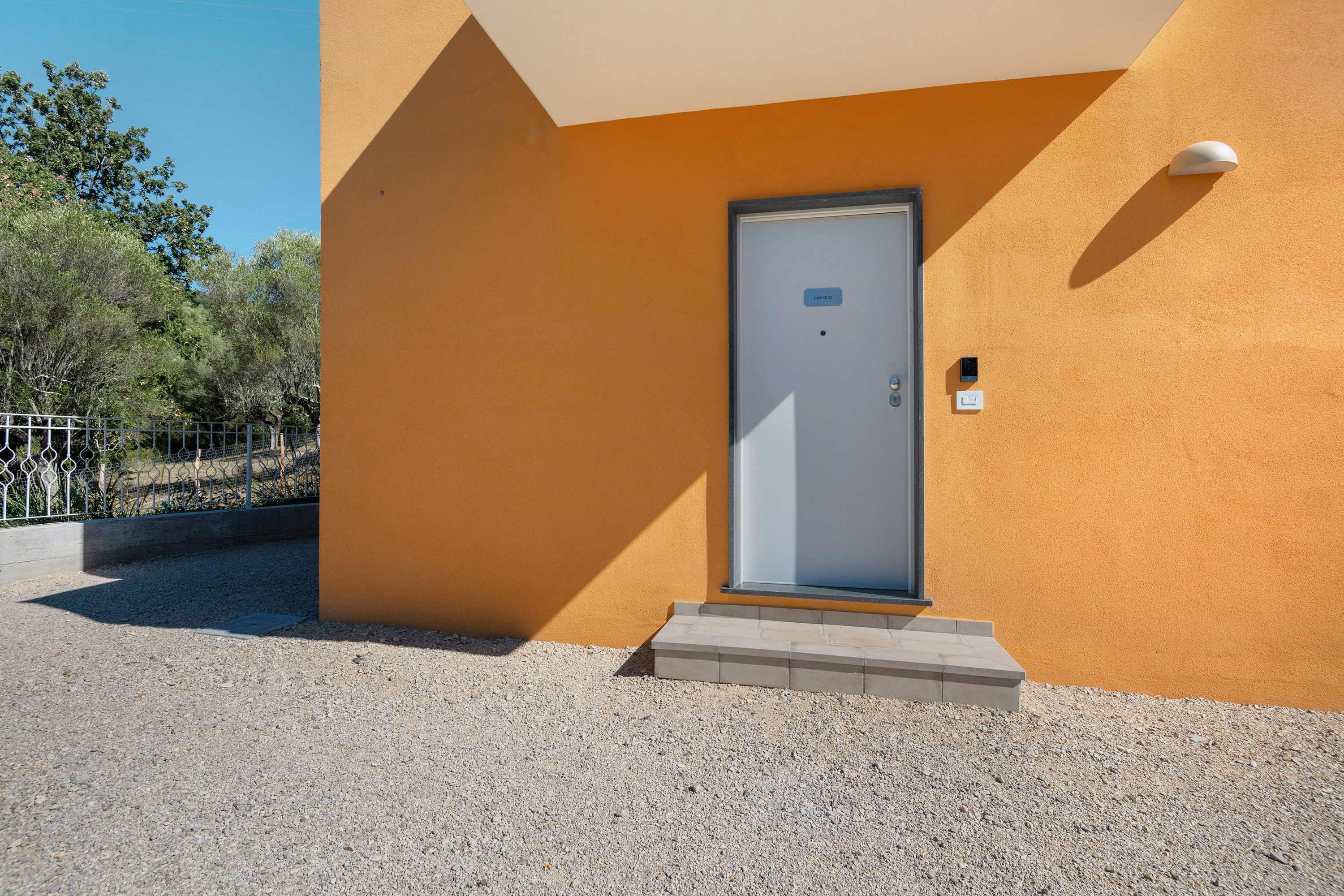 A building with a single door, a small step leading to it, and a security camera mounted on the wall.