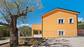 Un bâtiment à deux étages avec une façade jaune, une entrée abritée et une allée gravillonnée.